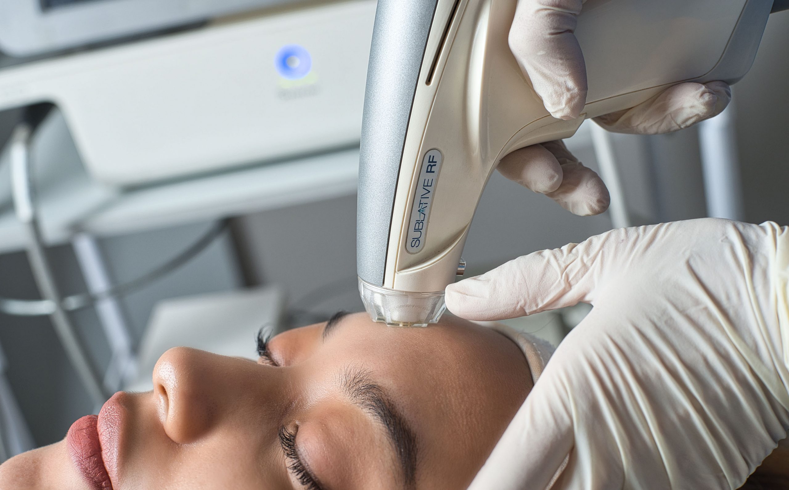 An aesthetician performing facial treatment on a patient, using laser.