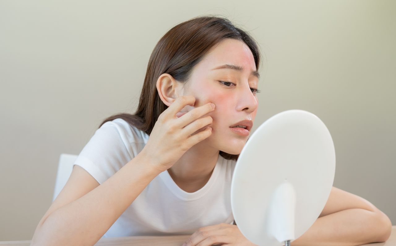 A woman appears frustrated as she tries to squeeze her acne. 