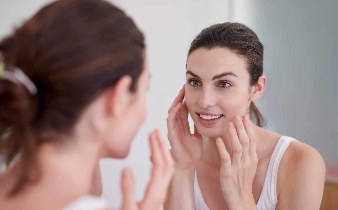 Woman with glowing skin looking at herself in the mirror, showcasing the effects of Profound Matrix treatment on skin texture and tone.