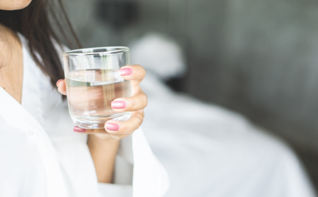 Woman holding a glass of water, emphasising hydration for glowing skin.