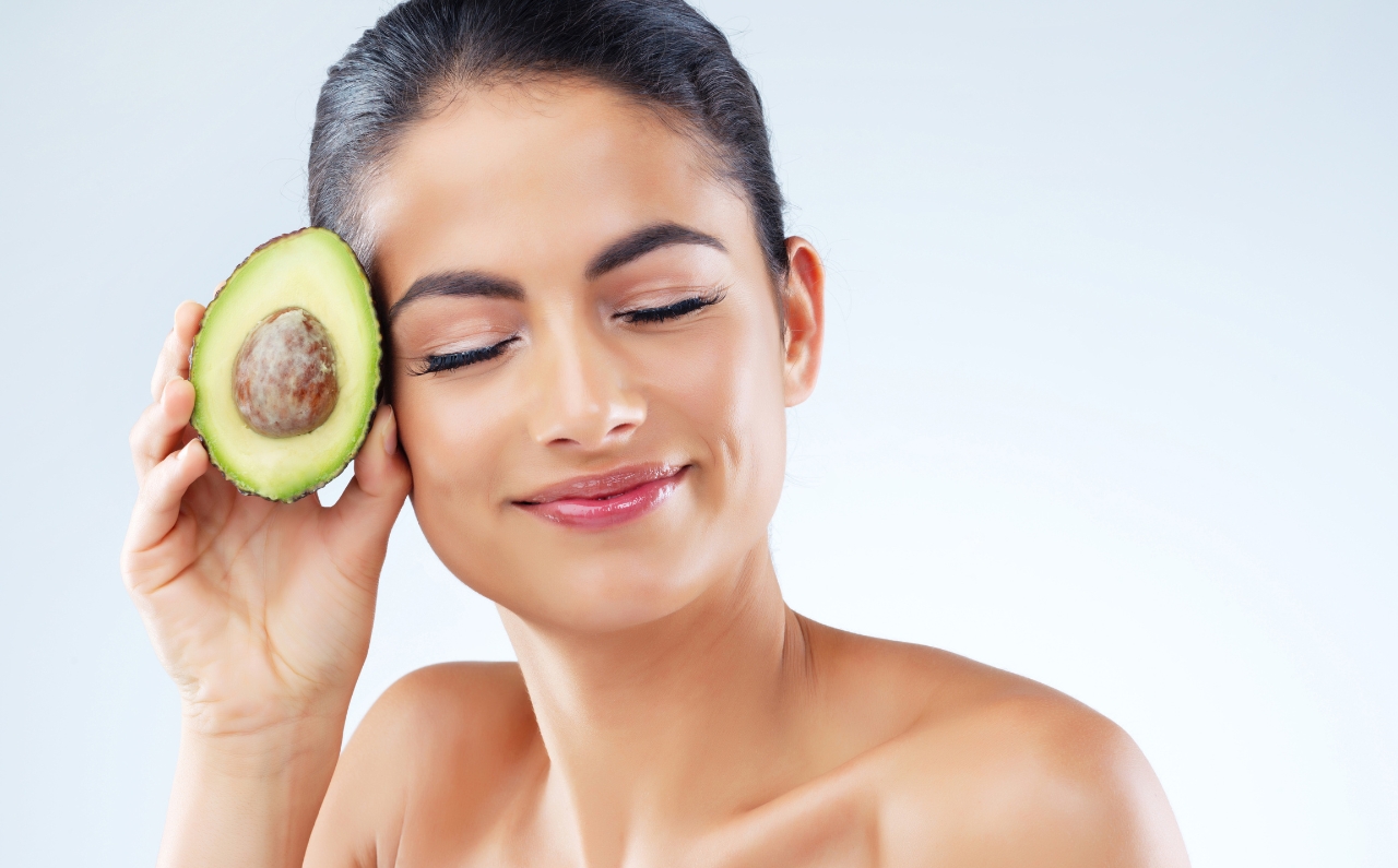 A woman holding a fresh avocado, symbolising nourishing skin from within.