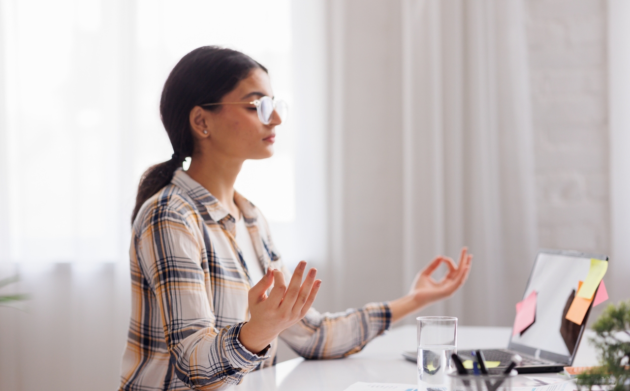 A woman meditating in a peaceful setting, focusing on relaxation and mindfulness to manage stress.