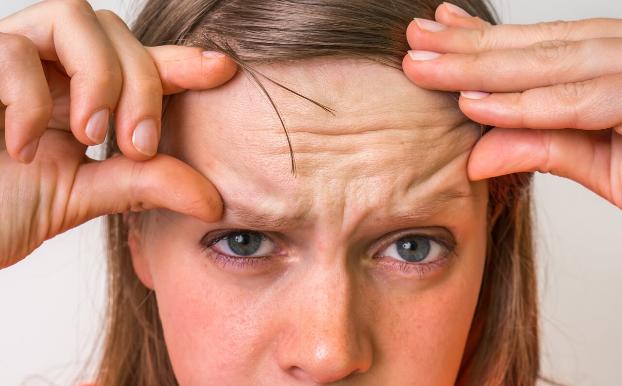 A woman pressing the folds of her forehead with a frustrated expression, illustrating the impact of stress and skin ageing.